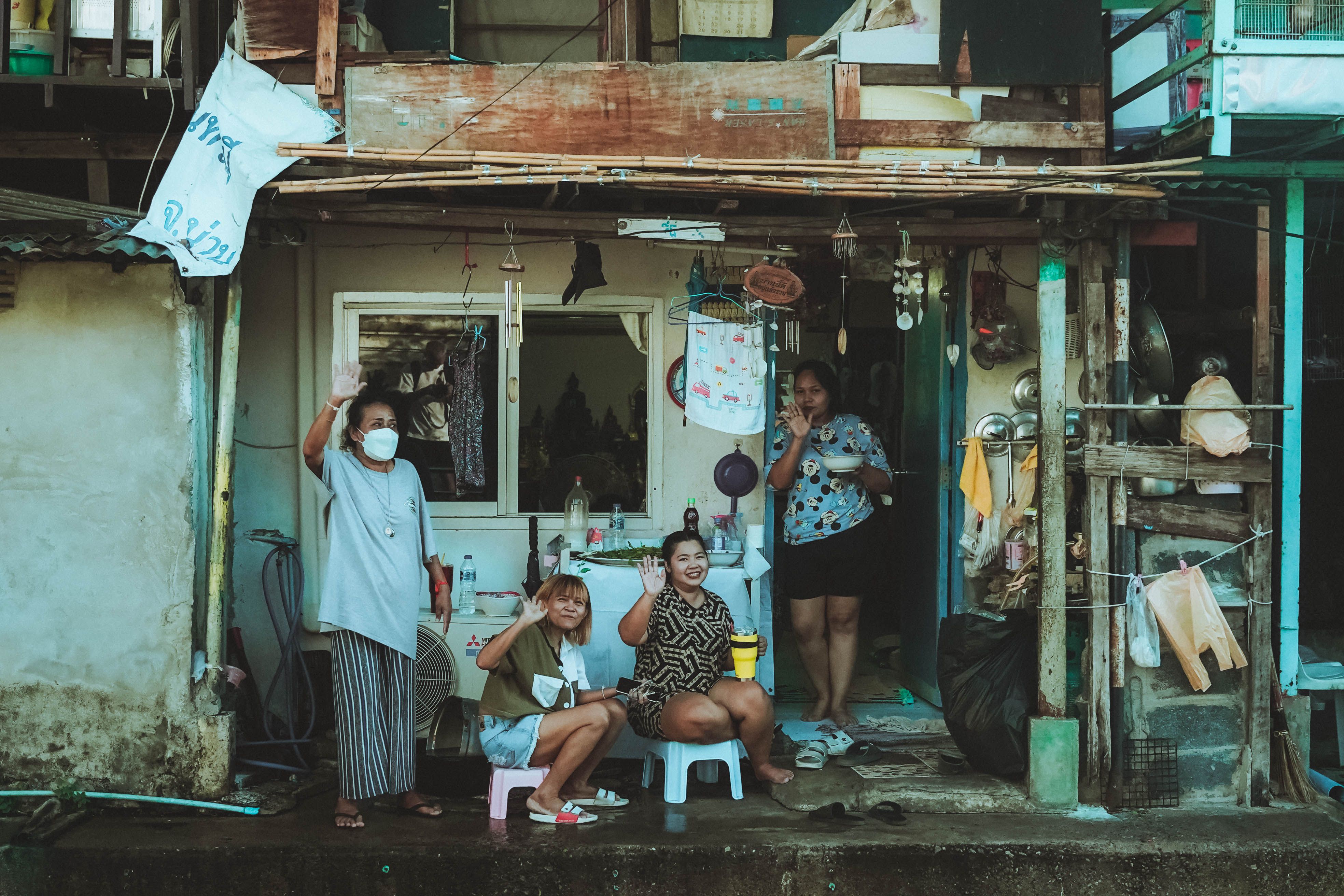 Women waving outside their home in a Bangkok urban neighborhood